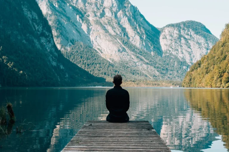 Man meditating on a wooden pier by a mountain lake
