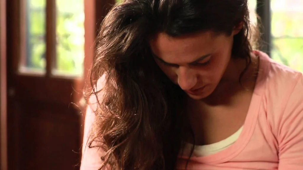 Still from the video Feldenkrais Moments: a woman with long dark hair looking down, absorbed in a movement