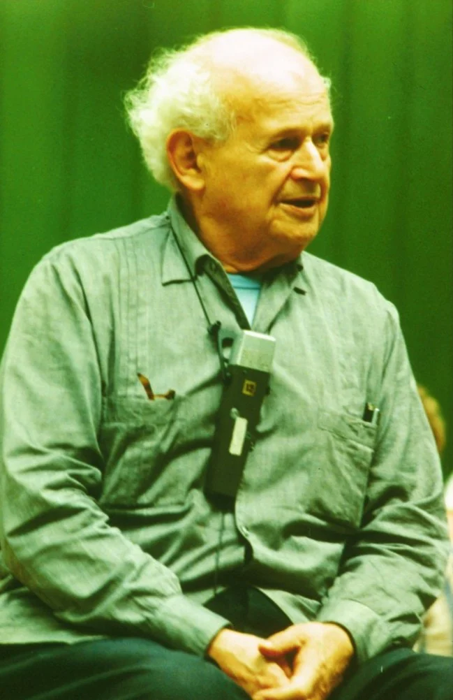 Moshe Feldenkrais in later life, seated and speaking, wearing a microphone